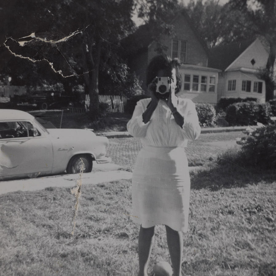 Black & white snapshot of a young Black woman dressed in white taking a photograph