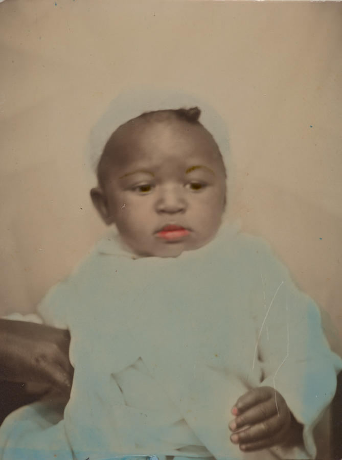 Black & white photograph of a baby, with its lips colored red and its clothes colored blue
