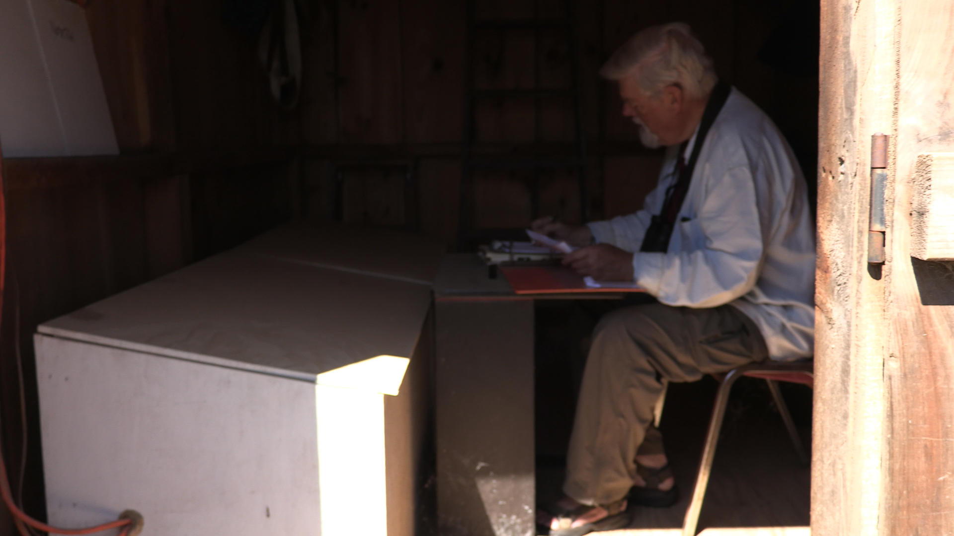Man sits at a table in a wooden shed in Cape Cod MA recording the wave information.