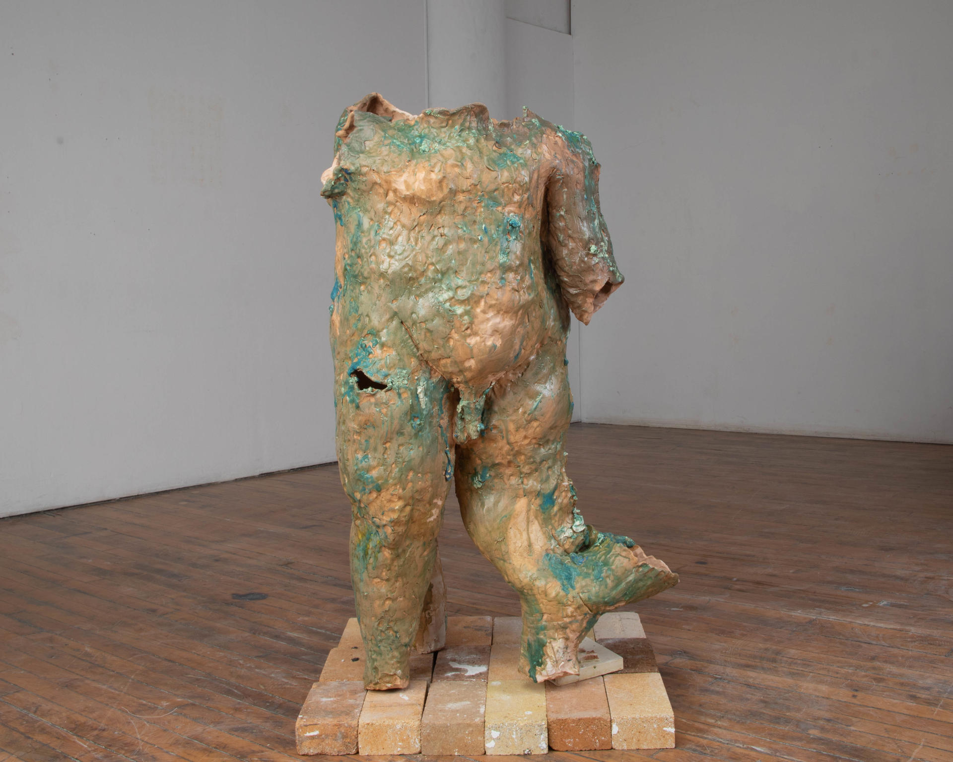 An enlarged and abject, hollow, ceramic body standing on top a small plinth of bricks