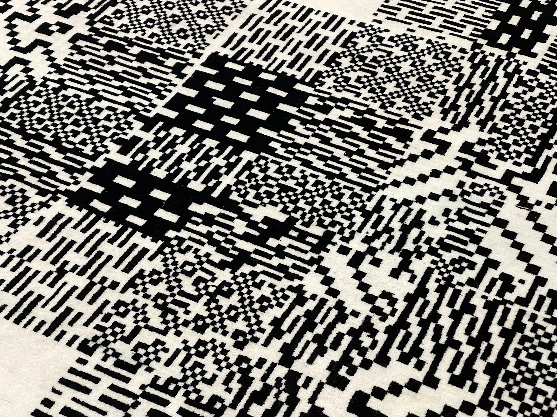 Detail documentation photograph of hand-knotted wool rug. The rug is covered in a semi-repetitive black and white patterned square image.