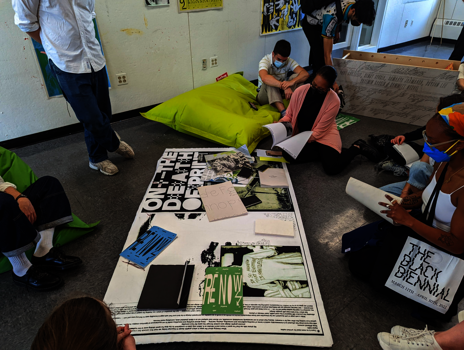 A group of people sit on the floor surrounding a poster covered by books
