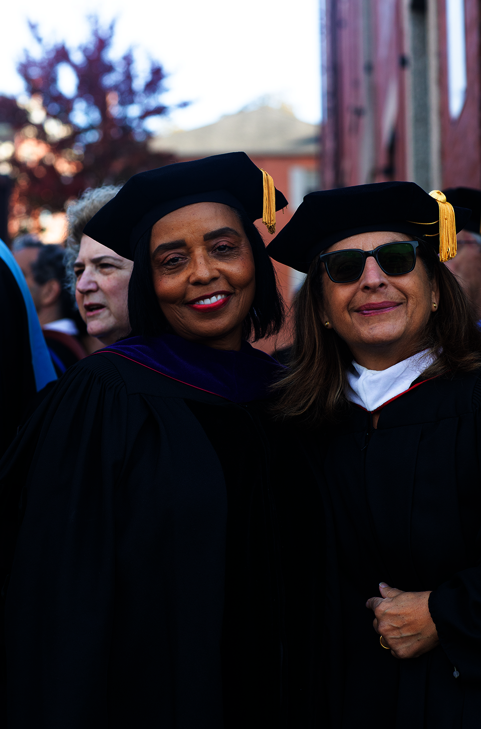 A Black woman and a white woman in sunglasses stand in doctoral robes, smiling.