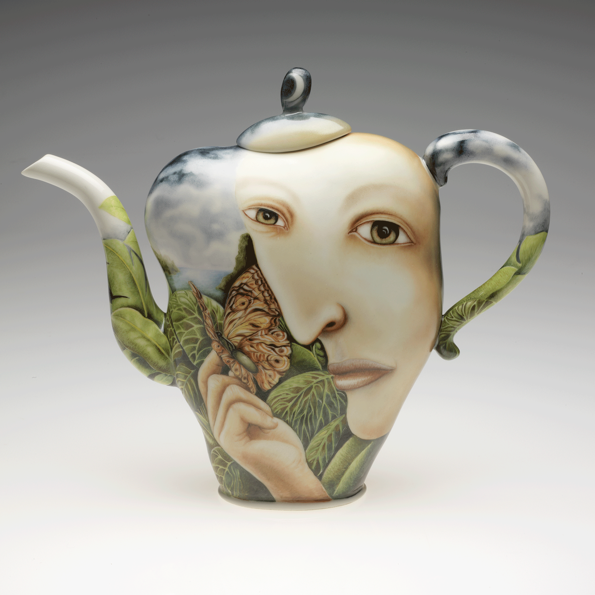 Teapot with spout facing left. It is painted with a large, light-skinned face and hand holding a black and orange butterfly, surrounded by tropical green leaves and cloudy blue sky