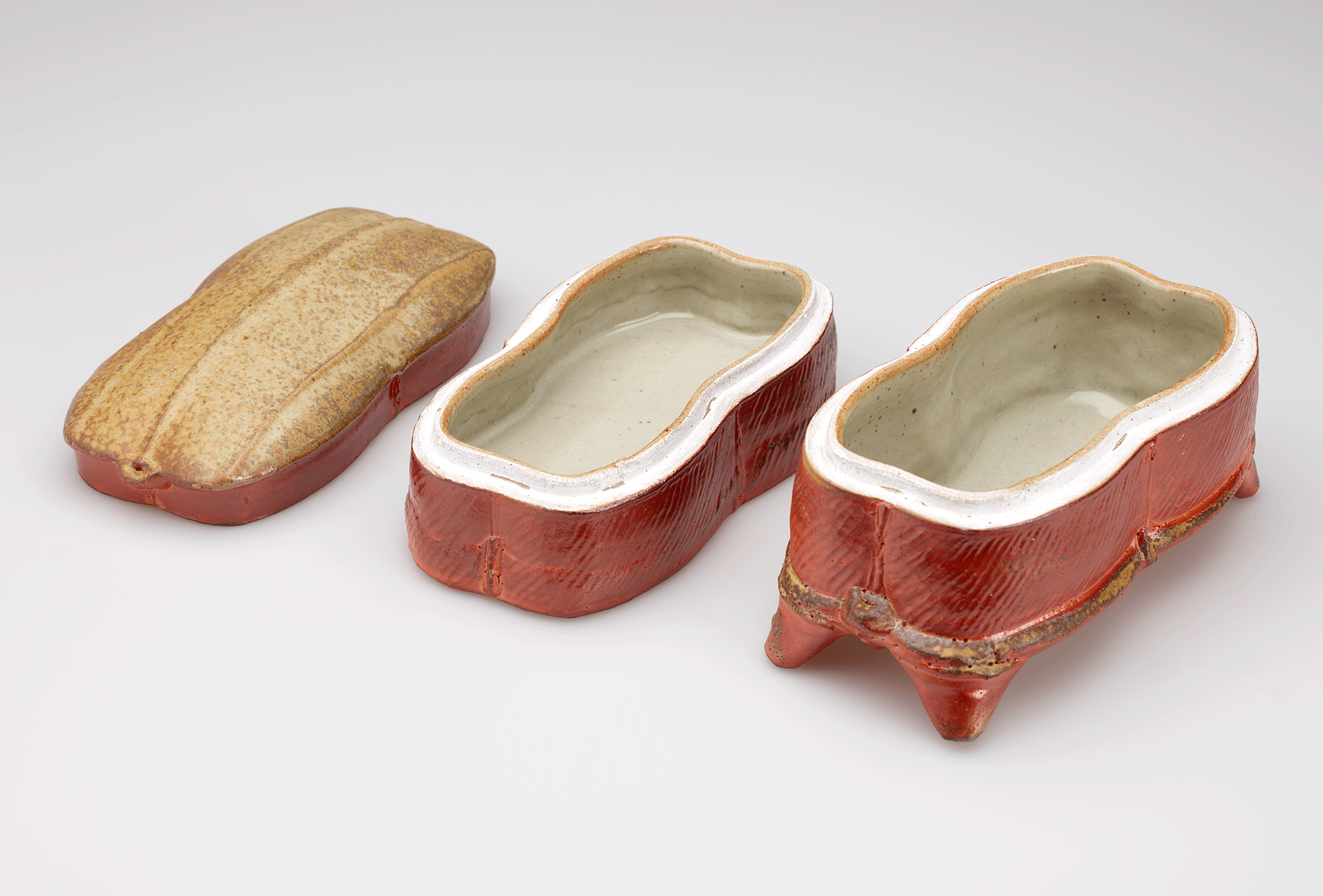 A rust-colored box with a light colored interior, triangular feet, and a tan top disassembled into three parts