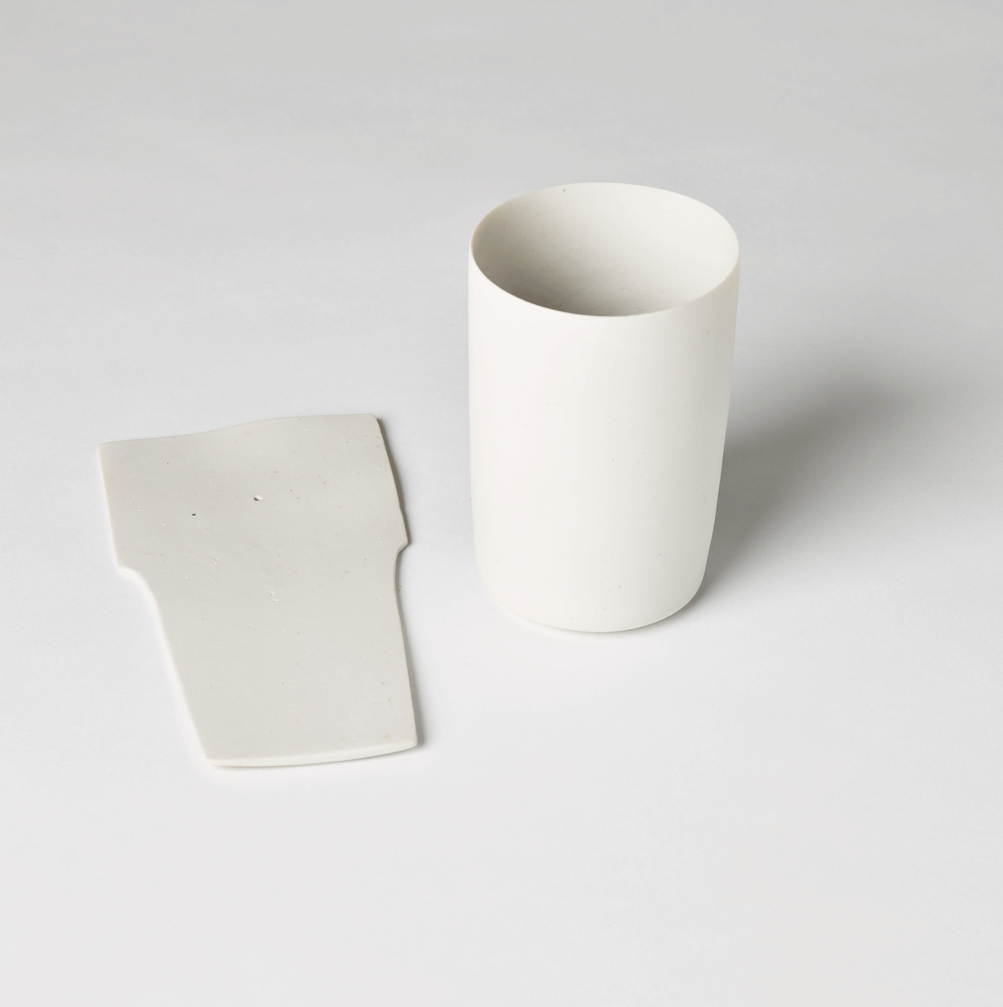 Thin, white slice of clay lying next to the white cup.