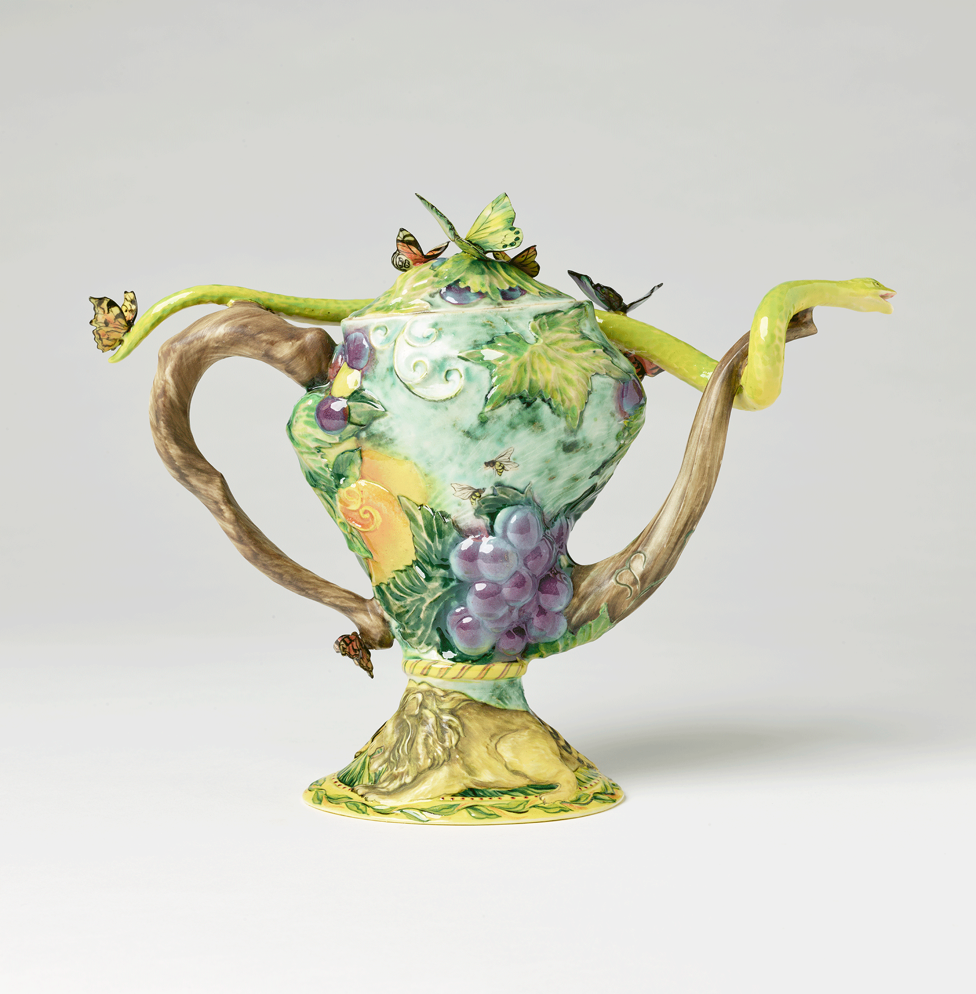 Opposite side of same teapot with leaves and grapes on body. Lion on the base. 3-dimensional butterflies on top of teapot and handle. Green 3-dimensional snake stretches from spout to handle.