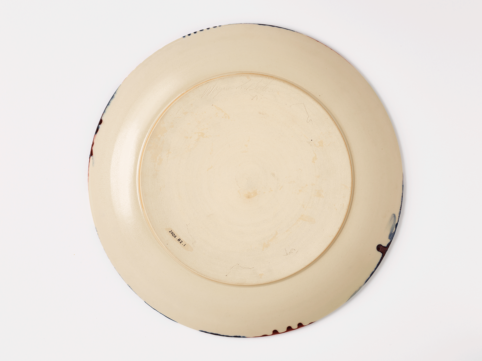 Underside of platter. Cream colored ground with drips of color around the edge. Accession number is visible.