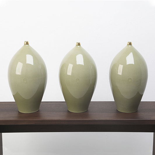 color photo; three shiny, jade-colored oblate ceramic vessels with golden tipped tops sit on a wooden table
