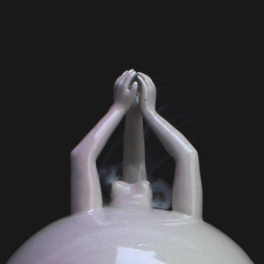 color photo; close of of a shiny pale ceramic sphere with a pink tinge. At the top, three delicate arms emerge and give each other a high-five. Below them, some smoke pours from an opening