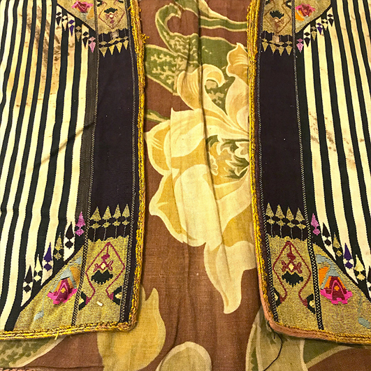 color photo; close up of a Syrian coat. The main fabric has a large floral motif, with stripes and geometric embroidery as accents