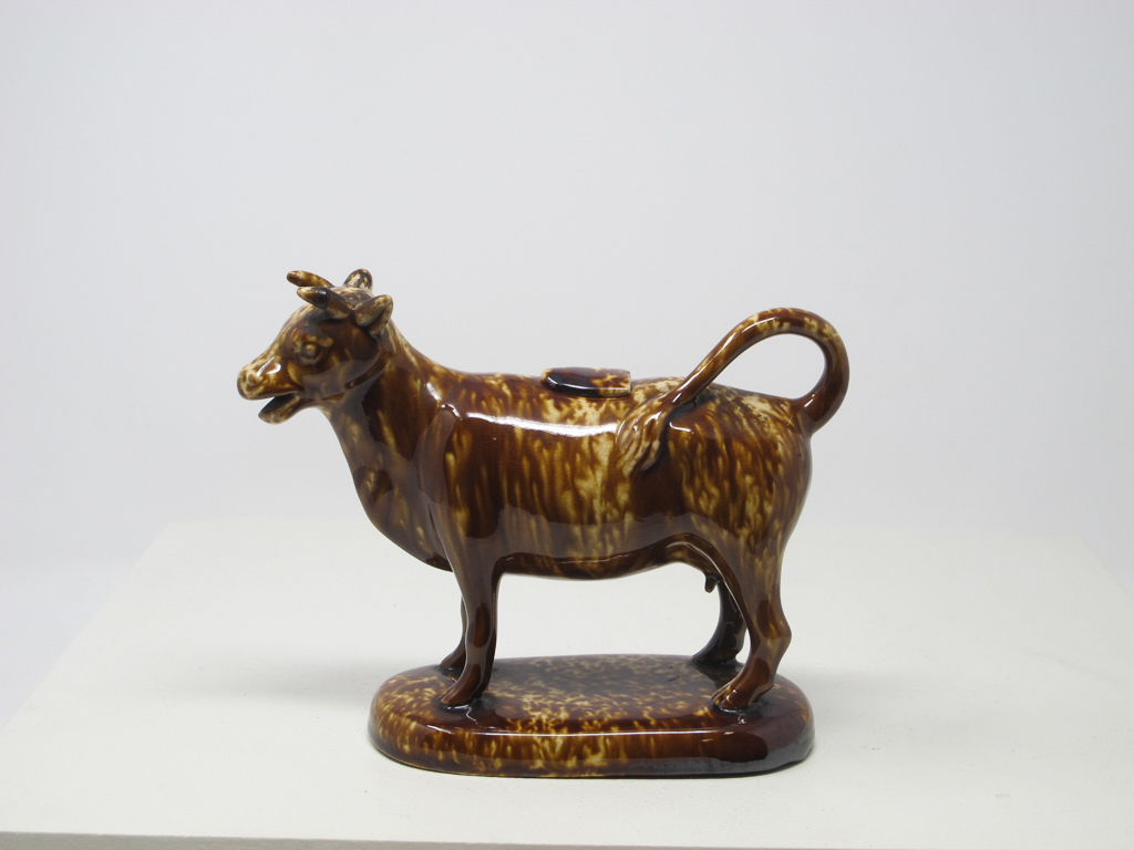 /A%20brown%20sculptural%20creamer%20in%20the%20shape%20of%20a%20cow%20with%20horns.%20There%20is%20a%20small%20flat%20lid%20in%20the%20center%20of%20its%20back.
