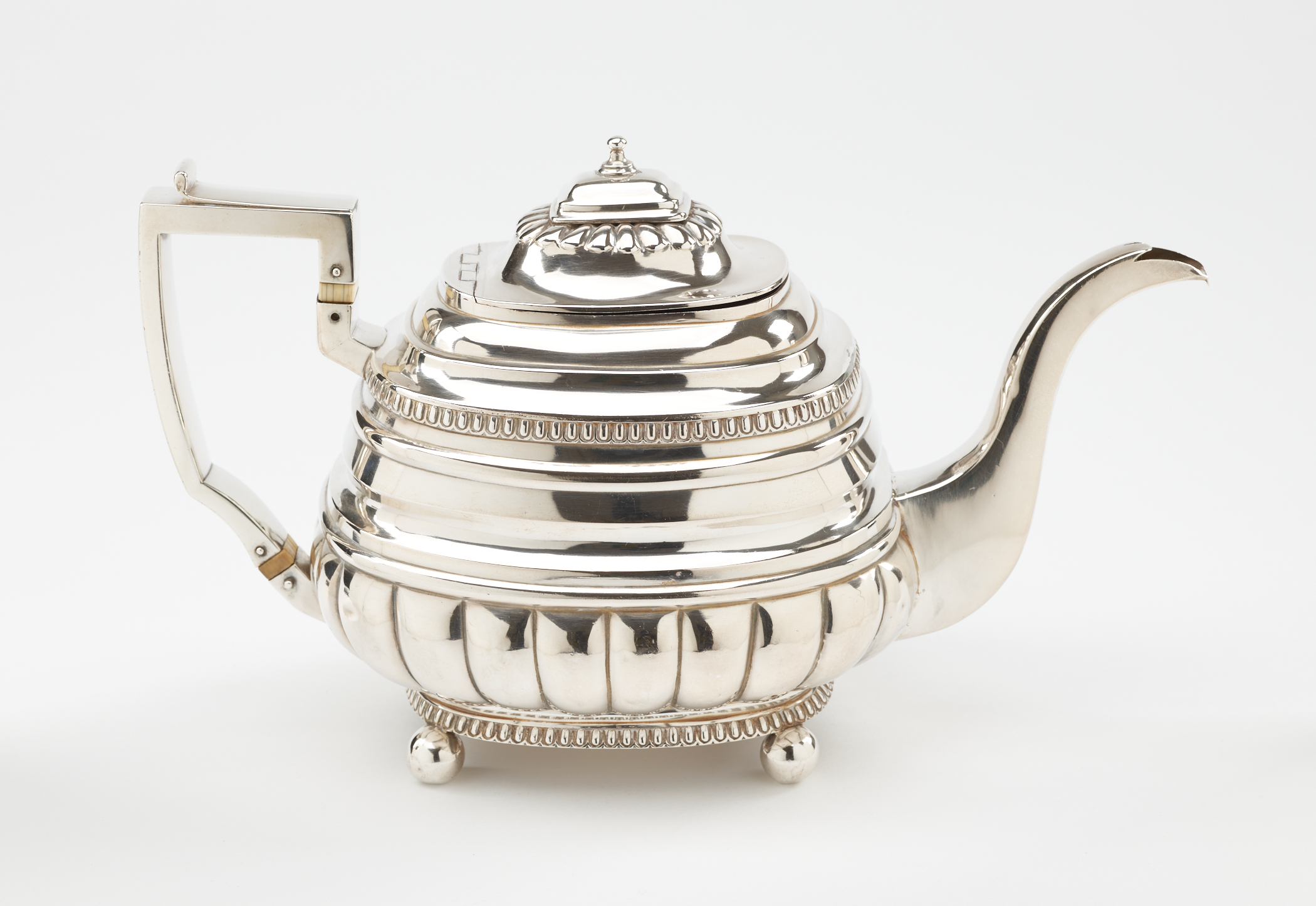 /A%20silver%20luster%20teapot%20with%20a%20decorative%20angular%20handle%2C%20a%20rounded%20square%20body%20and%20spout%20with%20sculptural%20decorations.