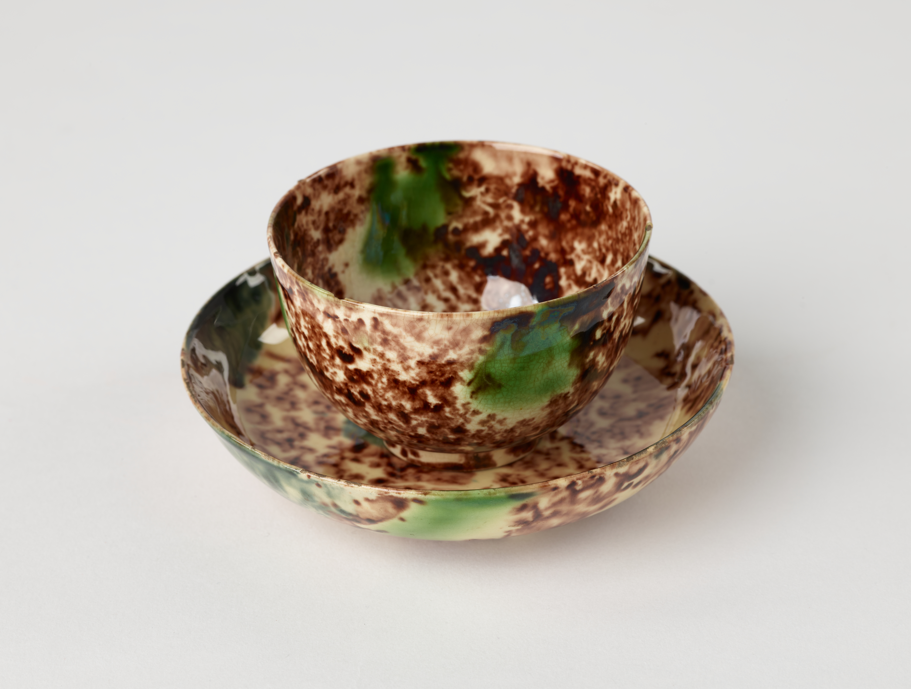 /A%20ceramic%20cup%20and%20saucer%20that%20is%20white%2C%20brown%2C%20and%20green%20in%20color.%20