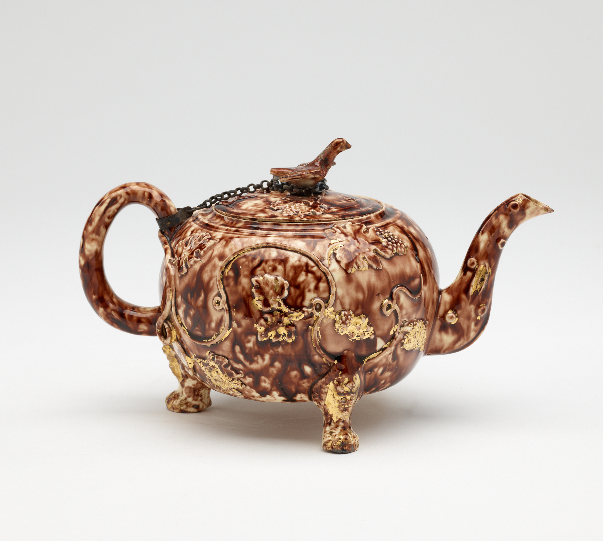 /A%20dark%20brown%20and%20white%20ceramic%20teapot%20with%20protruding%20feet%2C%20a%20spout%2C%20handle%2C%20and%20lid.%20The%20finial%20on%20the%20lid%20is%20connected%20to%20the%20handle%20by%20a%20chain.