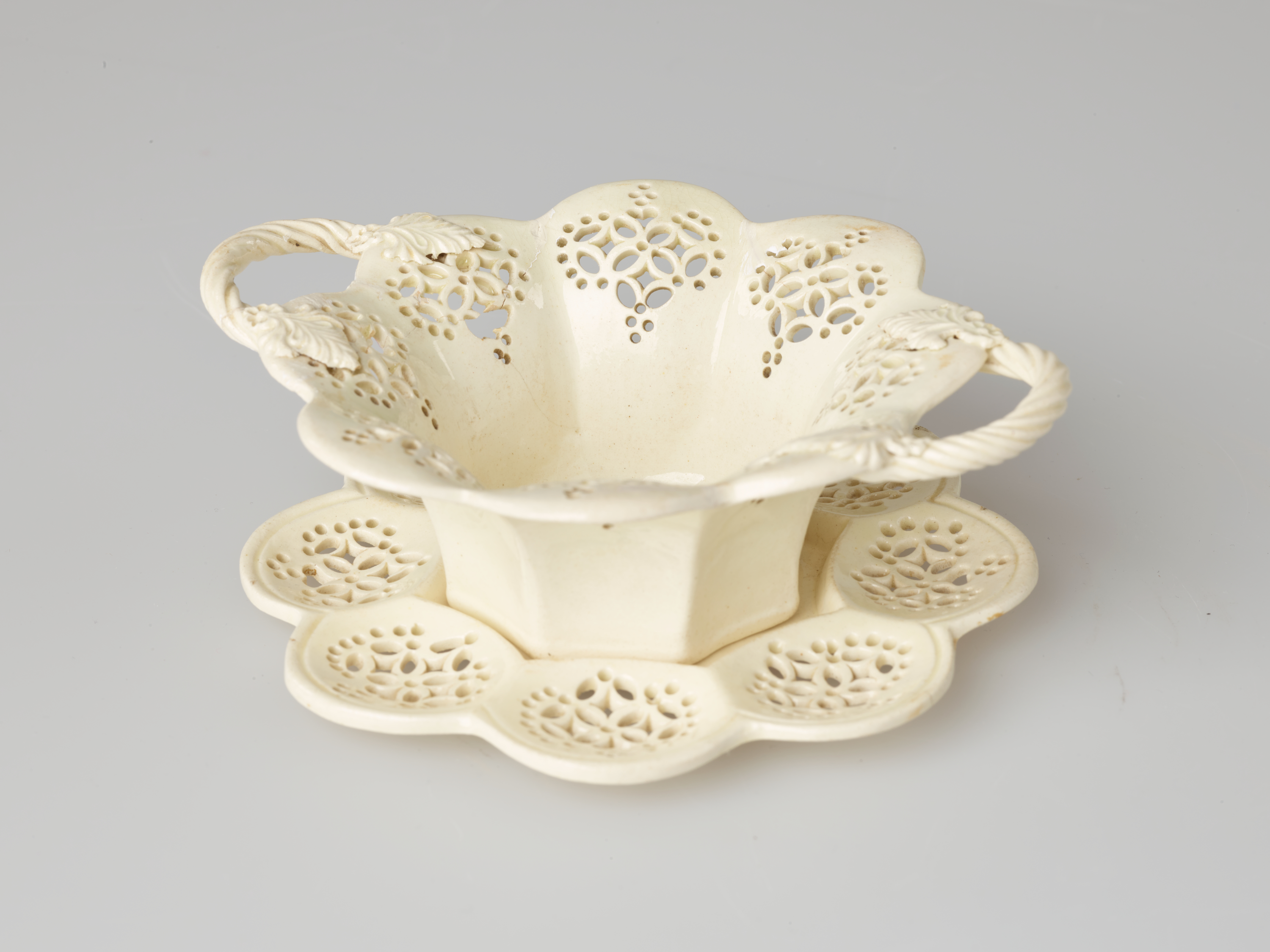 /A%20creamware%20sweetmeat%20dish%20with%20swirled%20handles%20and%20lace-like%20decorations%20cut%20into%20the%20octagonal%20vessel%20that%20is%20sitting%20on%20a%20matching%20tray.