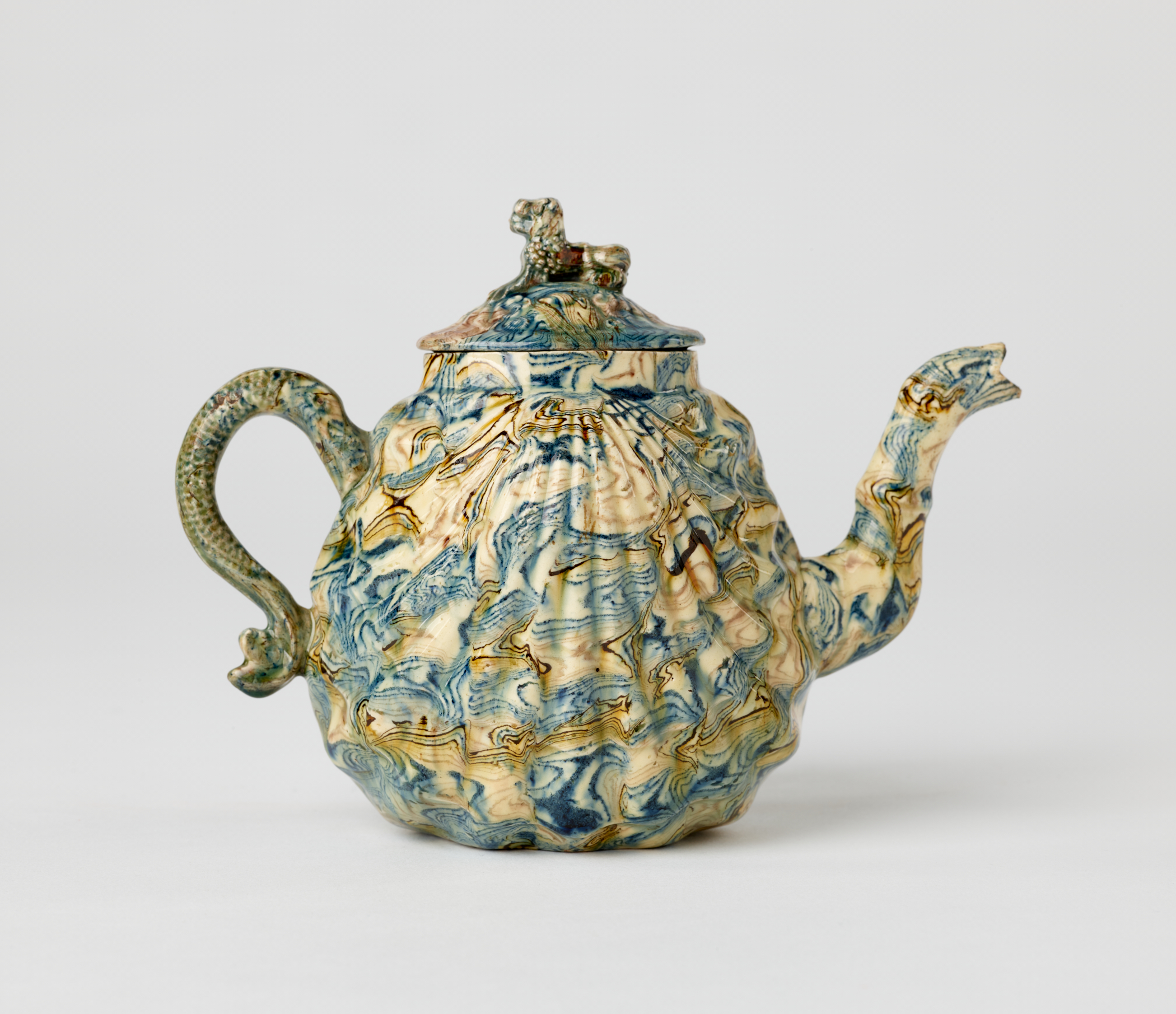 /A%20sculptural%20agateware%20teapot%2C%20with%20a%20sculptural%20fin%20handle%2C%20shell%20shaped%20body%2C%20decorative%20spout%2C%20and%20animal%20sculpted%20finial%20for%20the%20lid.%20It%20is%20blue%2C%20brown%2C%20and%20cream%20in%20color.