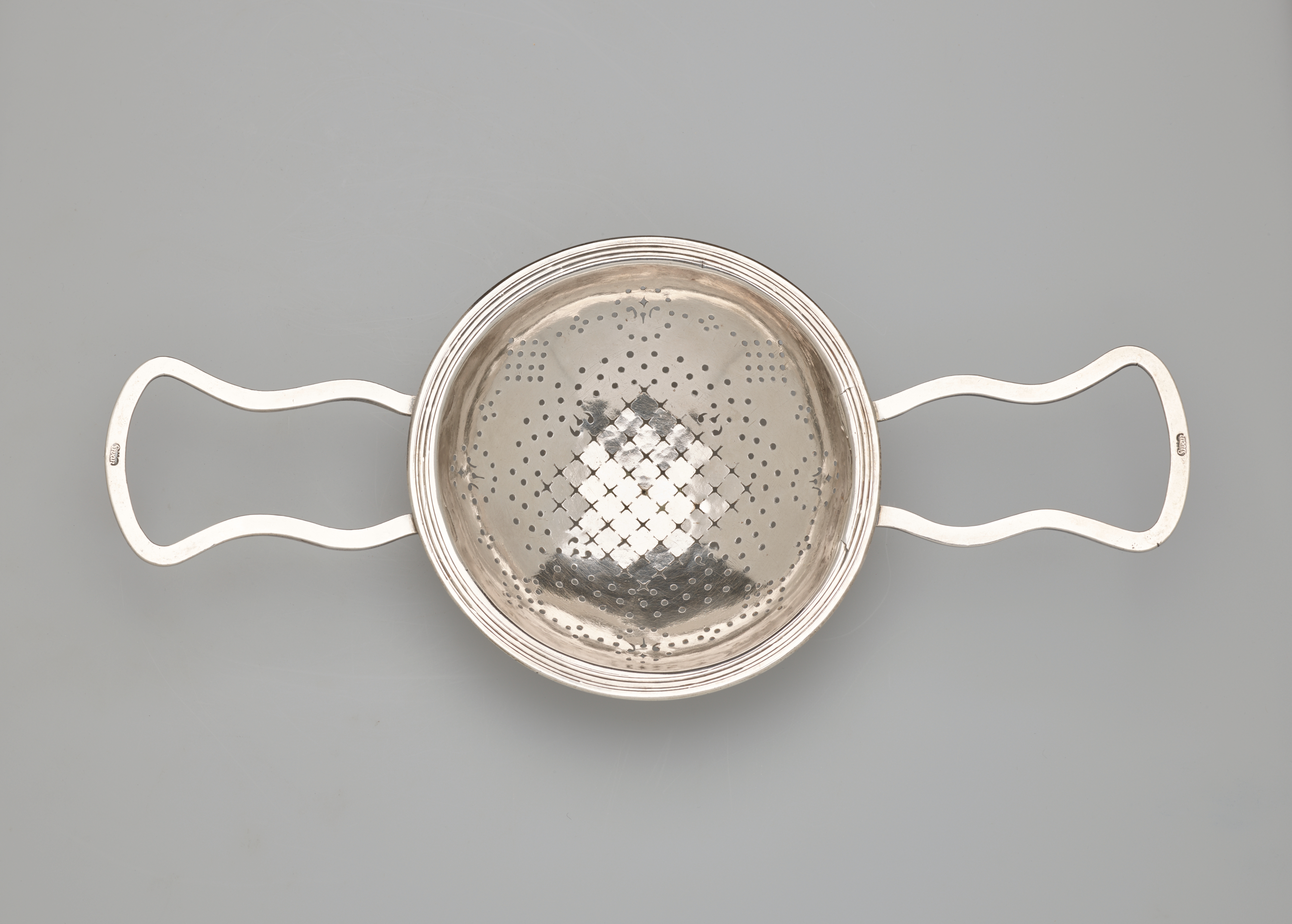 /A%20round%20silver%20strainer%20with%20symmetrical%20undulating%20handles.
