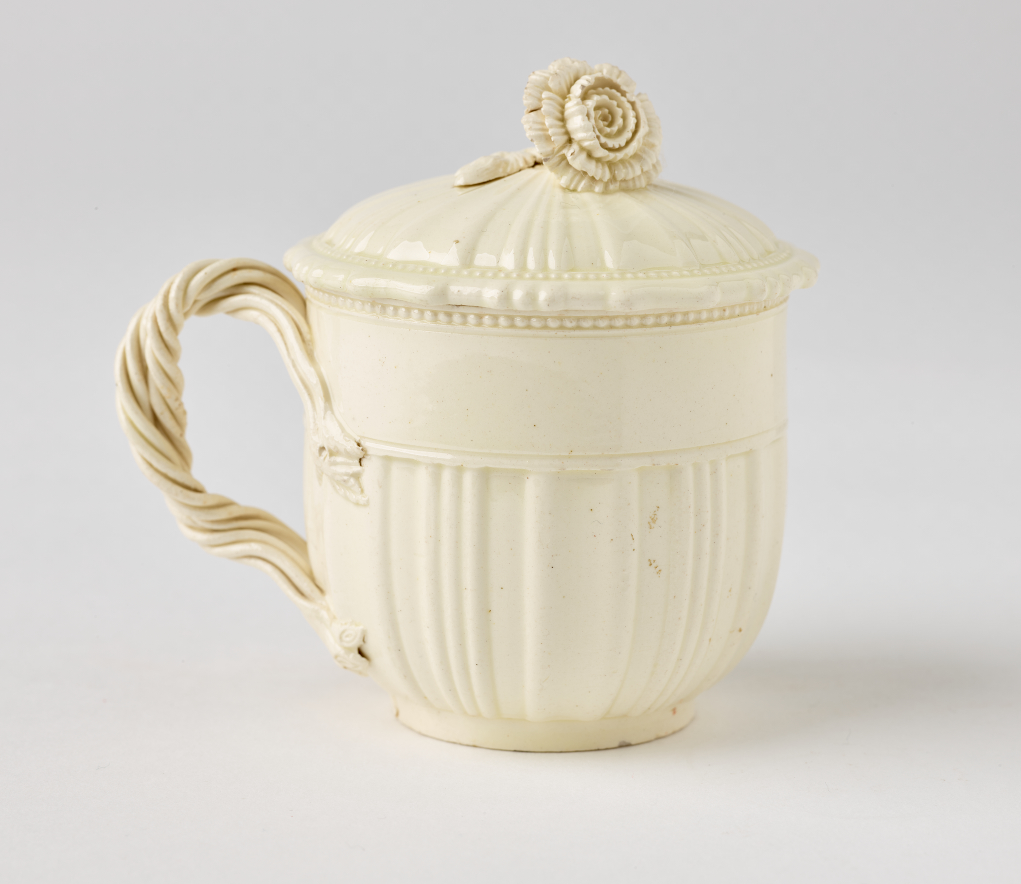 /A%20white%20creamware%20custard%20cup%2C%20with%20a%20sculptural%20swirled%20handle%2C%20and%20lid%20with%20sculpted%20finial.