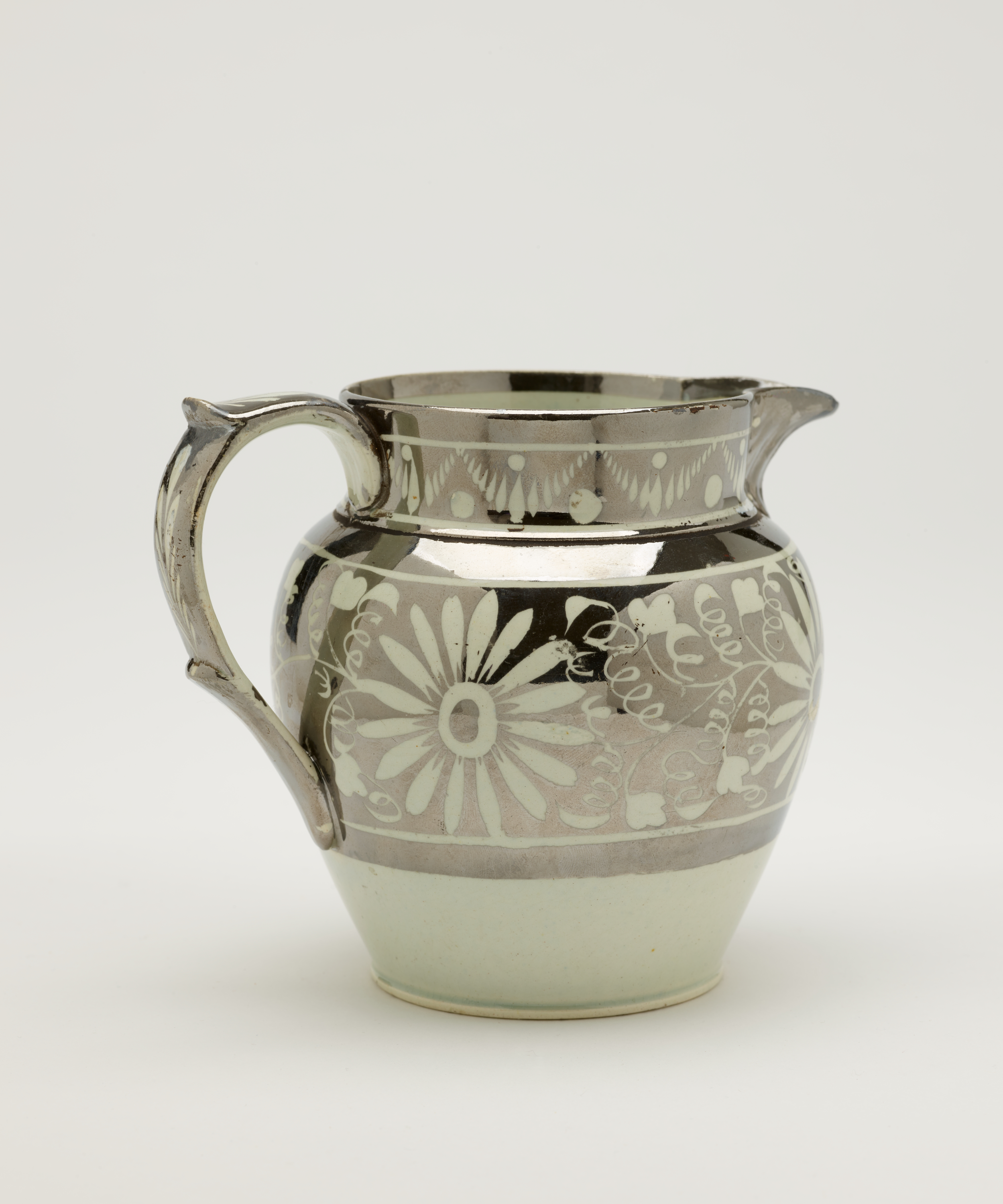 /A%20silver%20ceramic%20jug%20with%20a%20decorative%20handle%2C%20there%20are%20decorative%20floral%20motifs%20on%20the%20body%20of%20the%20vessel.