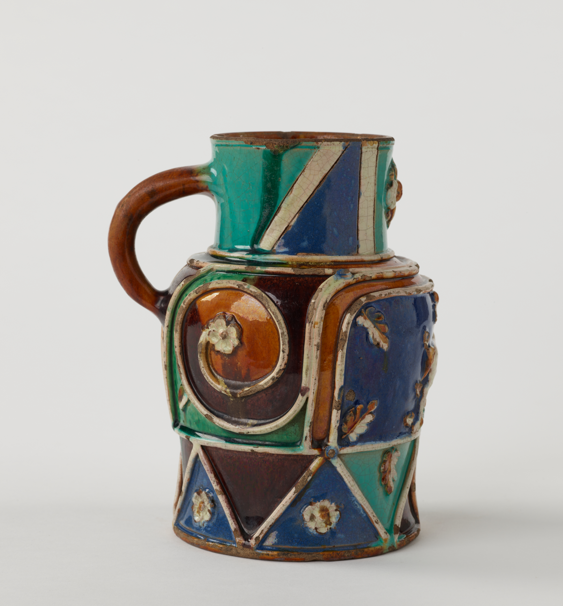 /A%20lead-glazed%20earthenware%20pitcher%20with%20white%2C%20blue%2C%20turquoise%2C%20orange%2C%20and%20black%20decorations.%20Some%20of%20the%20white%20decorations%20are%20raised.%20