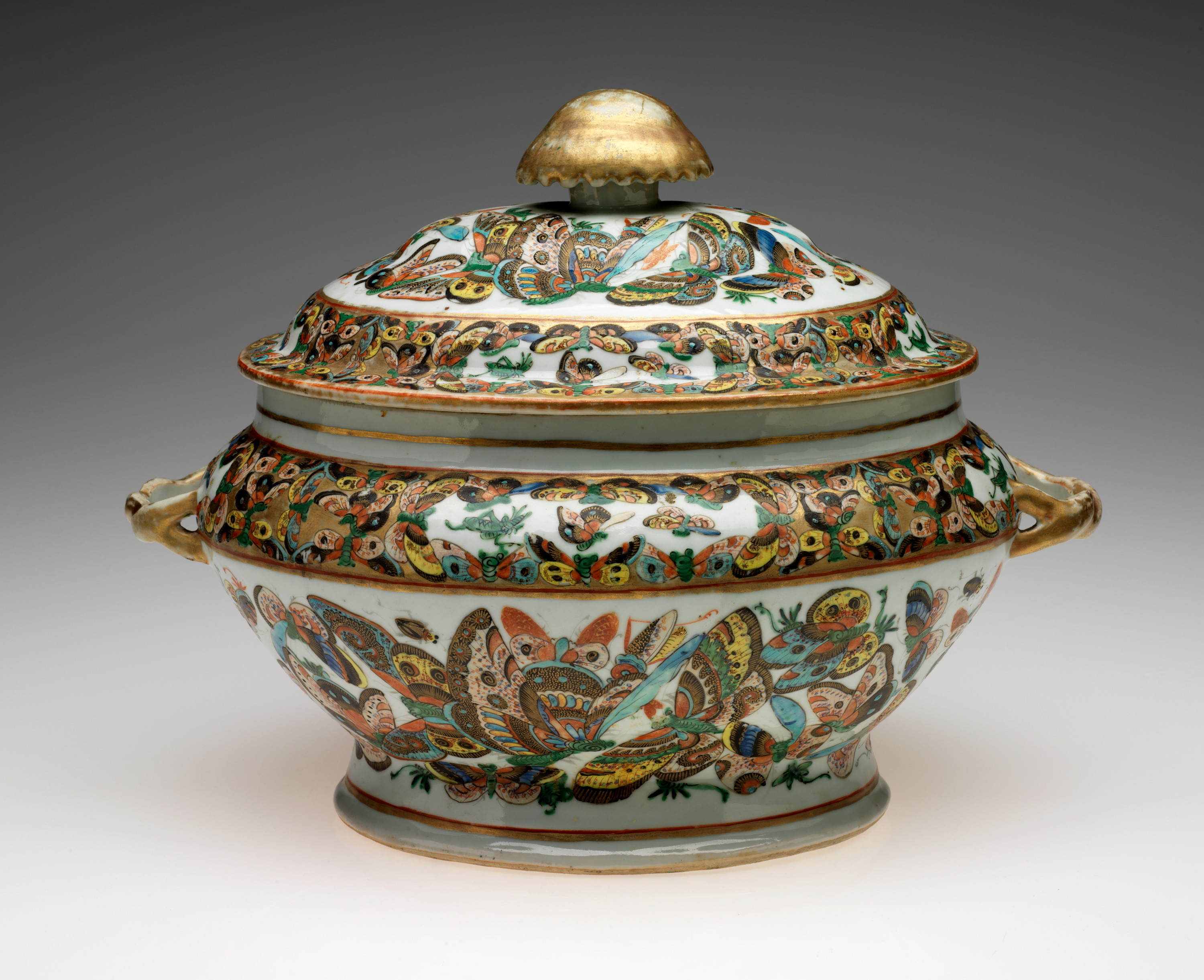 /An%20oval%20lidded%20vessel%20with%20a%20large%20gold%20finial.%20The%20body%20of%20the%20vessel%20is%20decorated%20with%20multicolored%20butterflies%20on%20a%20white%20ground.%20