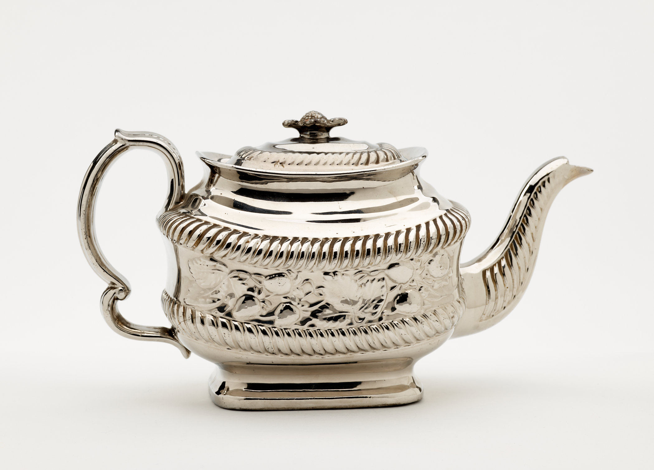 /A%20silver%20luster%20teapot%20with%20a%20decorative%20handle%2C%20a%20rounded%20square%20body%20and%20spout%20with%20sculptural%20decorations.