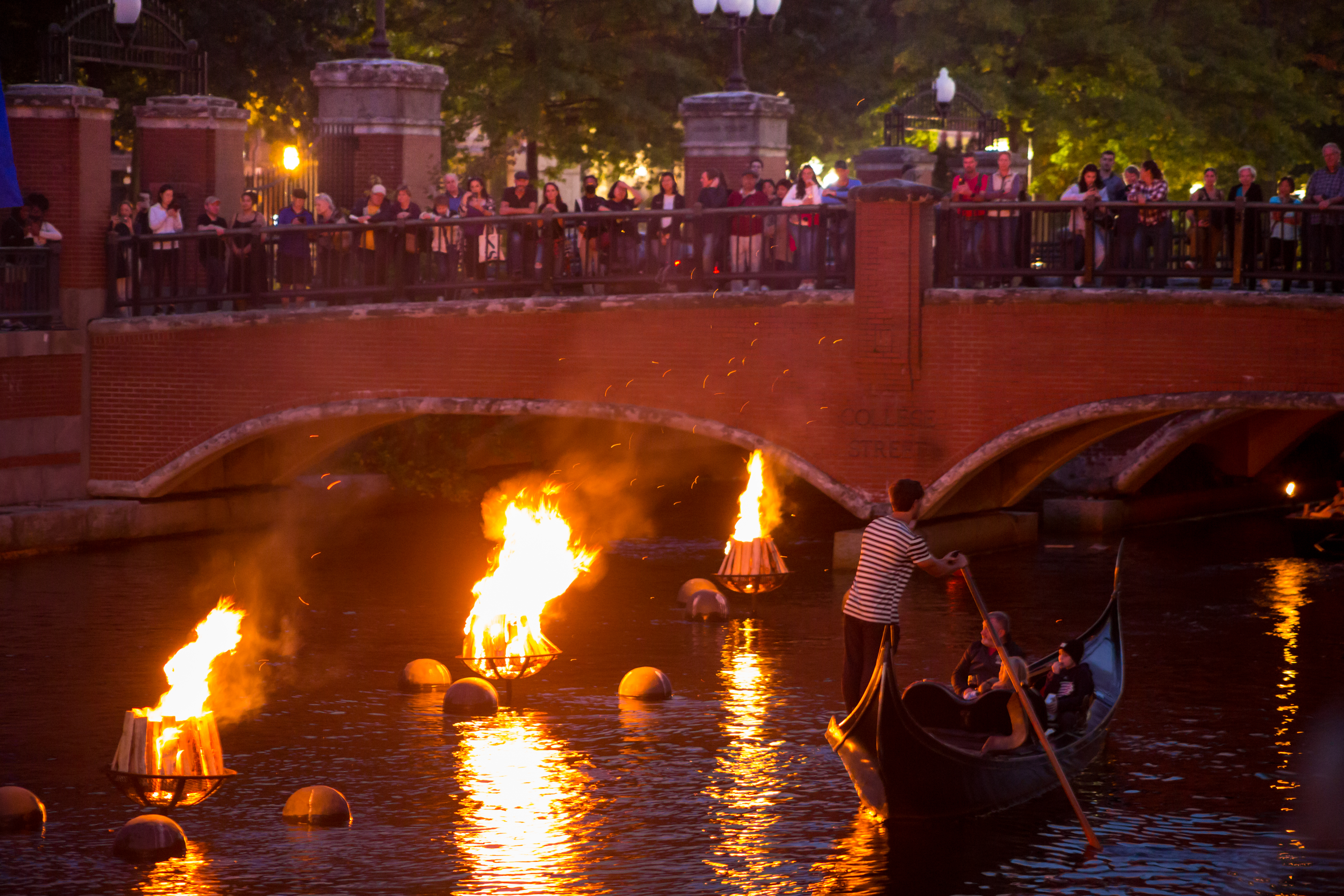 /Providence%20WaterFire.%20At%20night%2C%20a%20crowd%20gathers%20on%20the%20College%20Street%20bridge%20overlooking%20the%20Providence%20River.%20The%20river%20is%20lit%20by%20burning%20braziers.%20A%20man%20rows%20a%20gondola%20under%20the%20bridge.