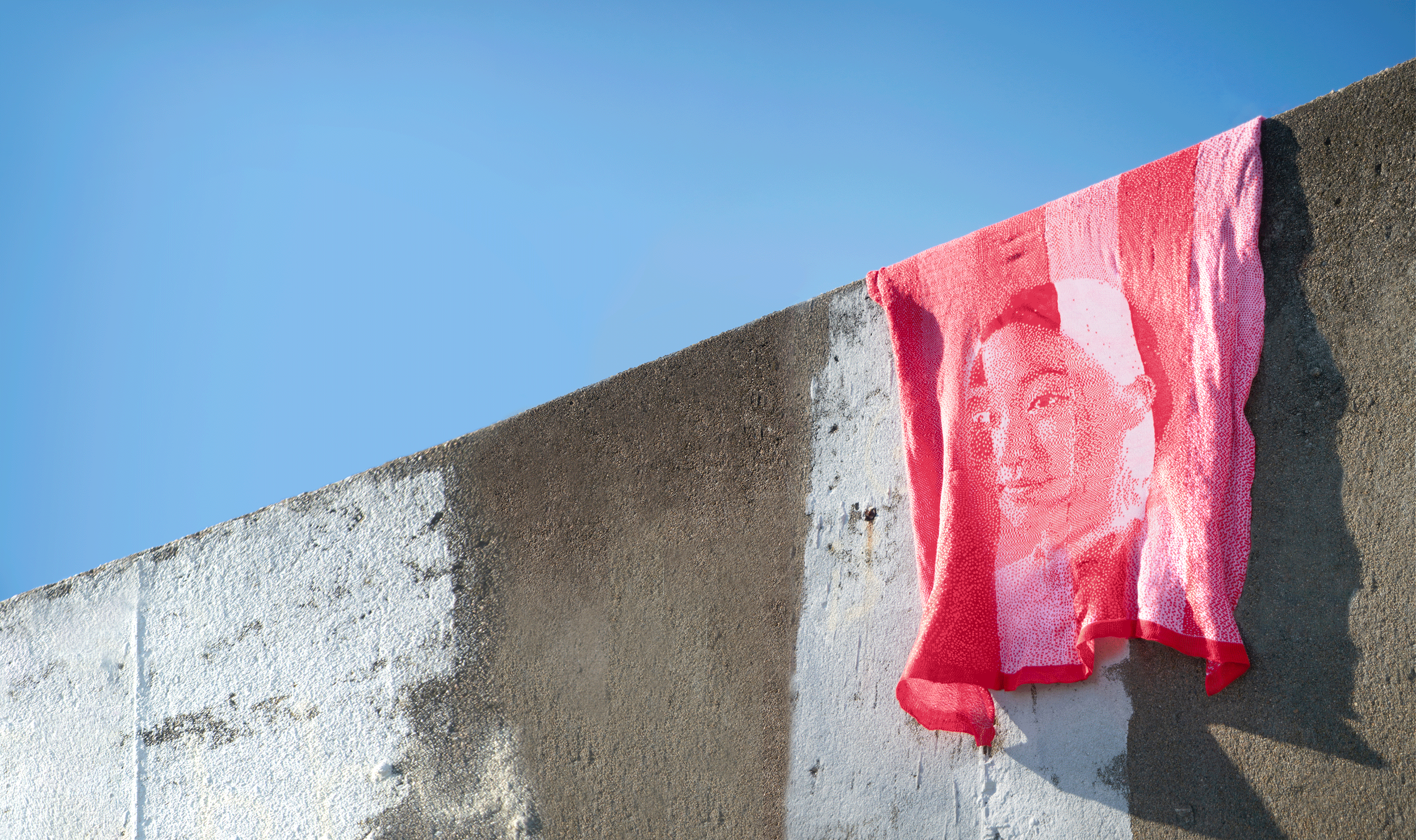 A knitted blanket in red and pink blowing in the wind. The blanket shows face of the artist.