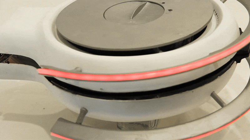 A white cooking appliance is opened, and a hand uses a fork to remove a pancake from the cooking surface.