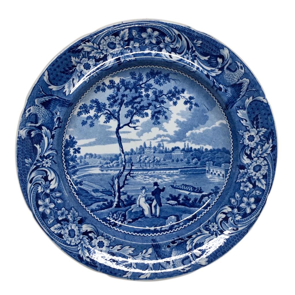 blue and white transferware plate depicting a scene near Philadelphia with two figures sitting by a tree, looking at a waterway