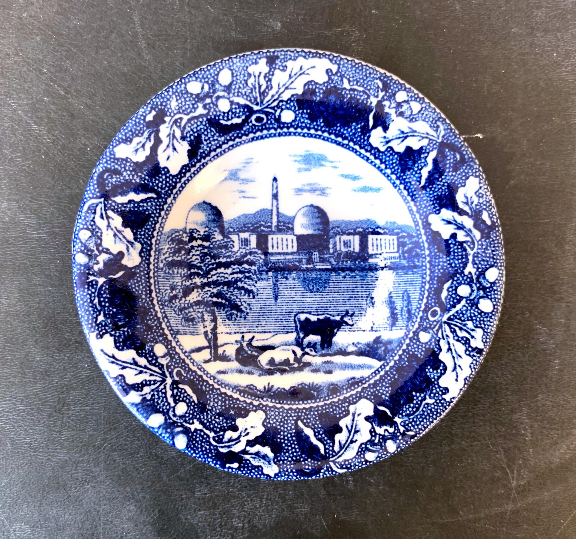 blue and white transferware cup plate depicting a the indian point nuclear power plant and cows, with an oak leaf border