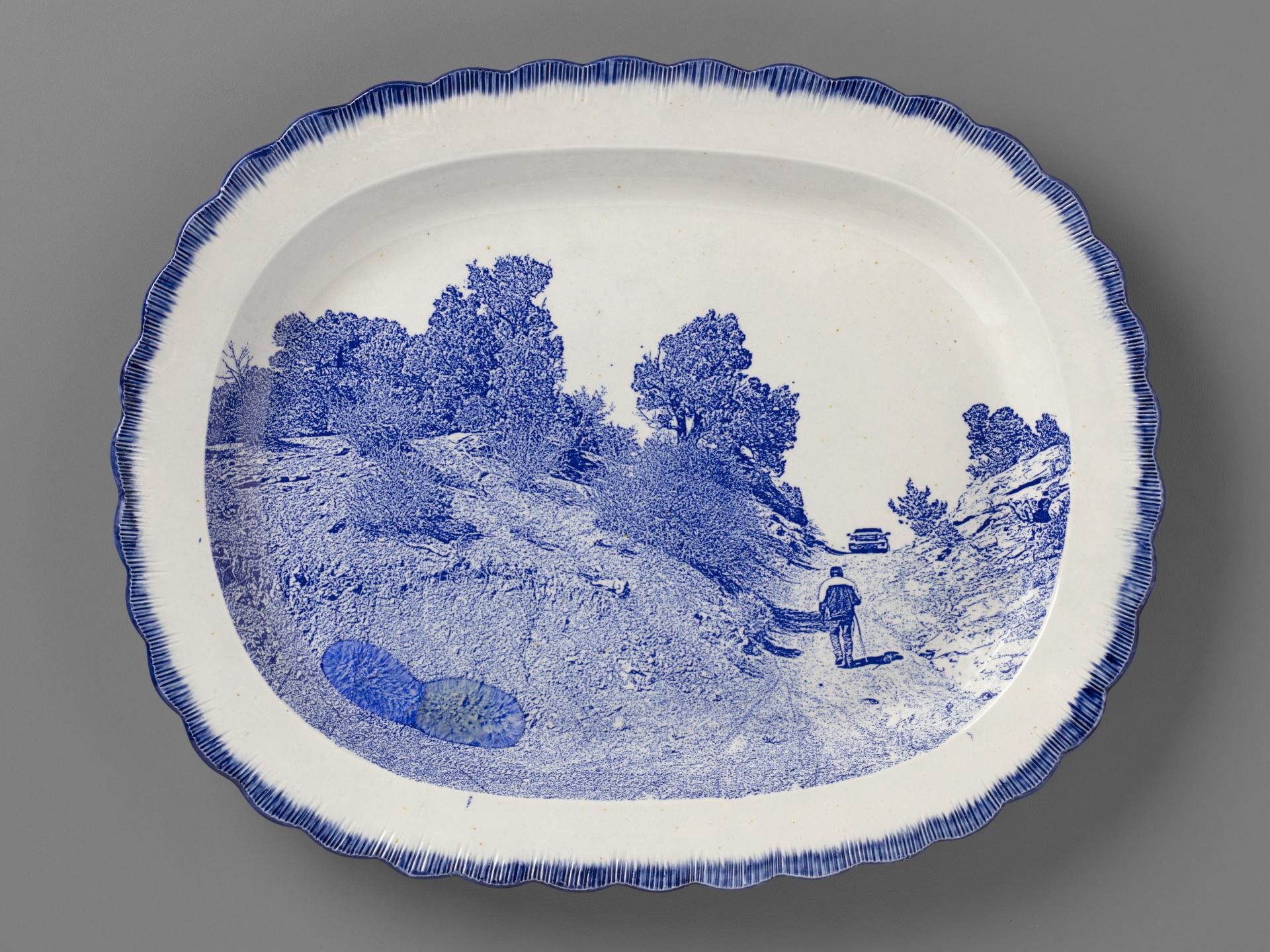 blue and white transferware plate depicting Timothy Benally walking up the road up to one of the Cove uranium mines, with melted Uranium glass