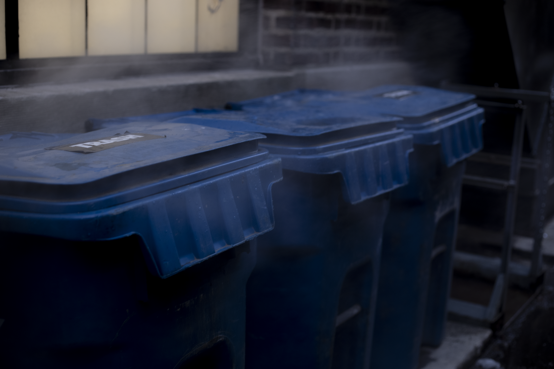 steam rises around three blue trash cans