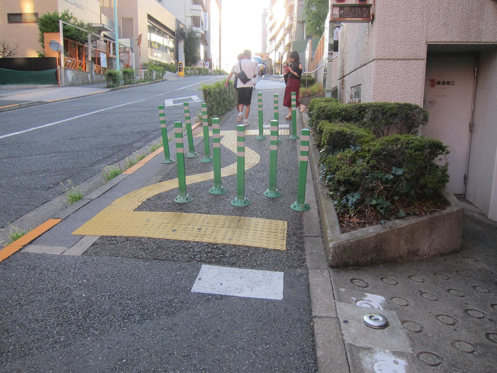 A curvy path of tactile pavement surrounded by green bollards