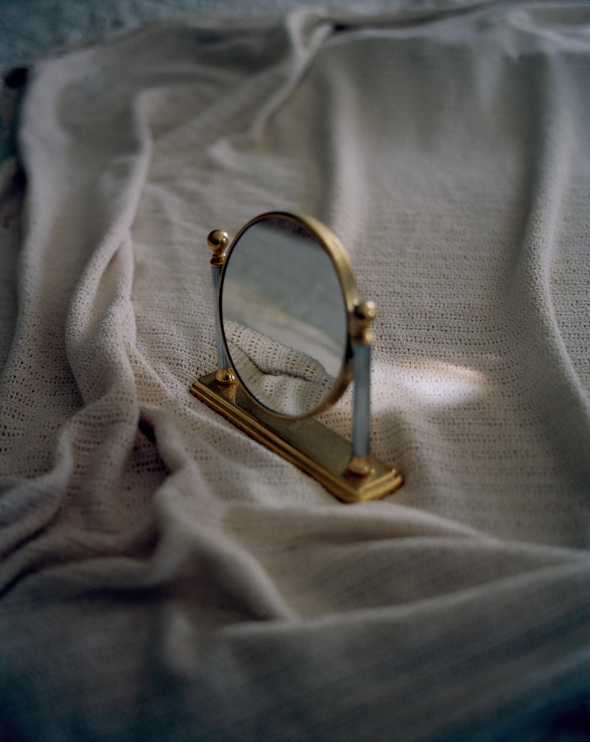 A small mirror stands on a bed, reflecting the rumpled sheets