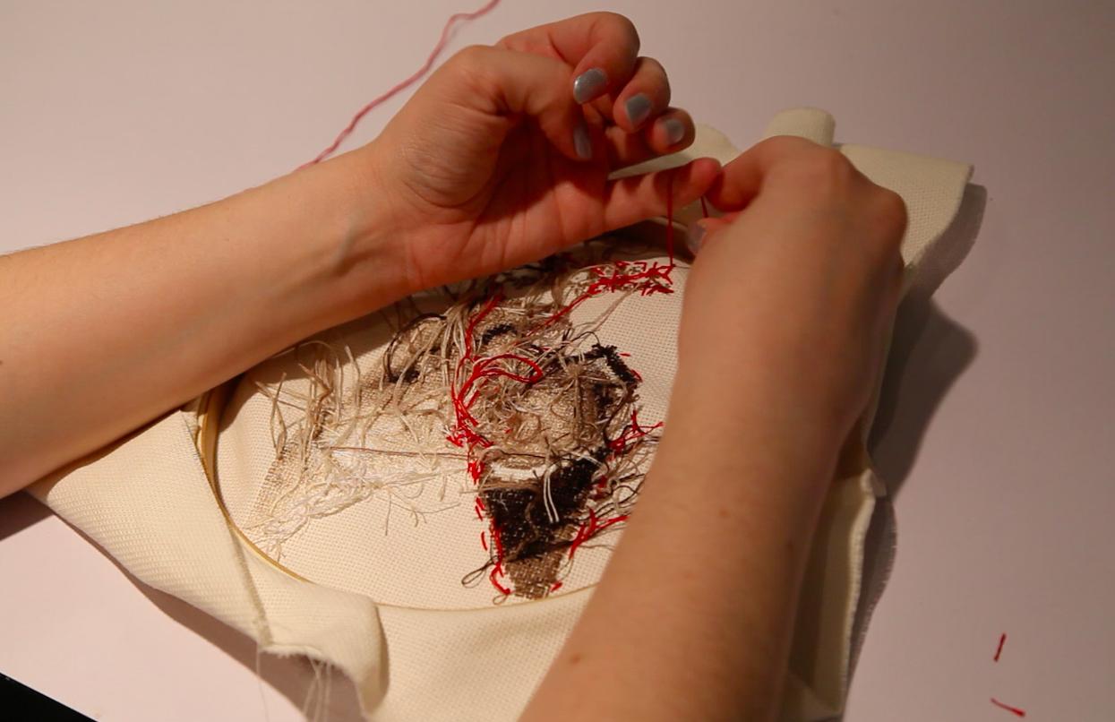 A person ties a knot on the back of an embroidery hoop