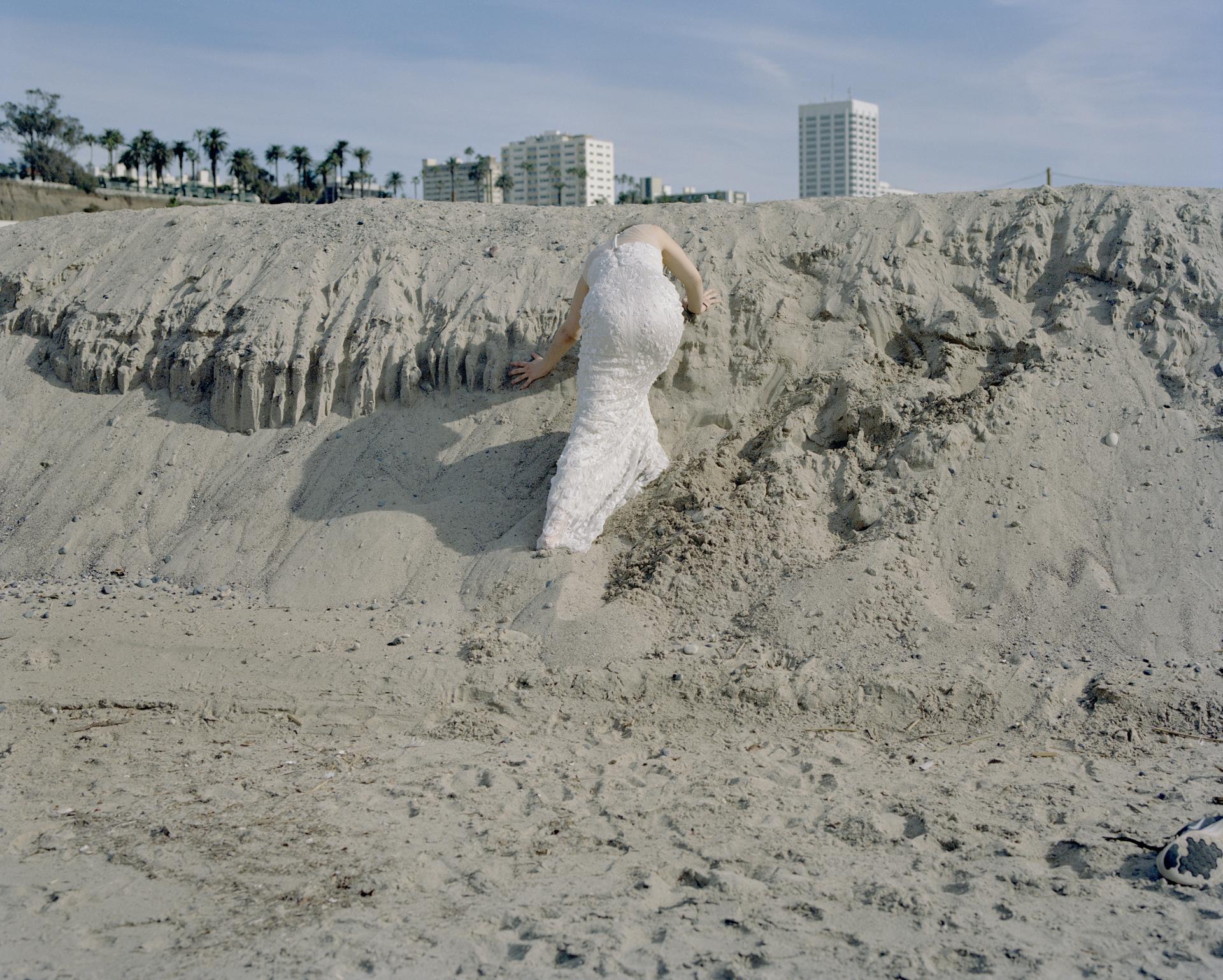 A woman climbing sand dunes in her wedding dress