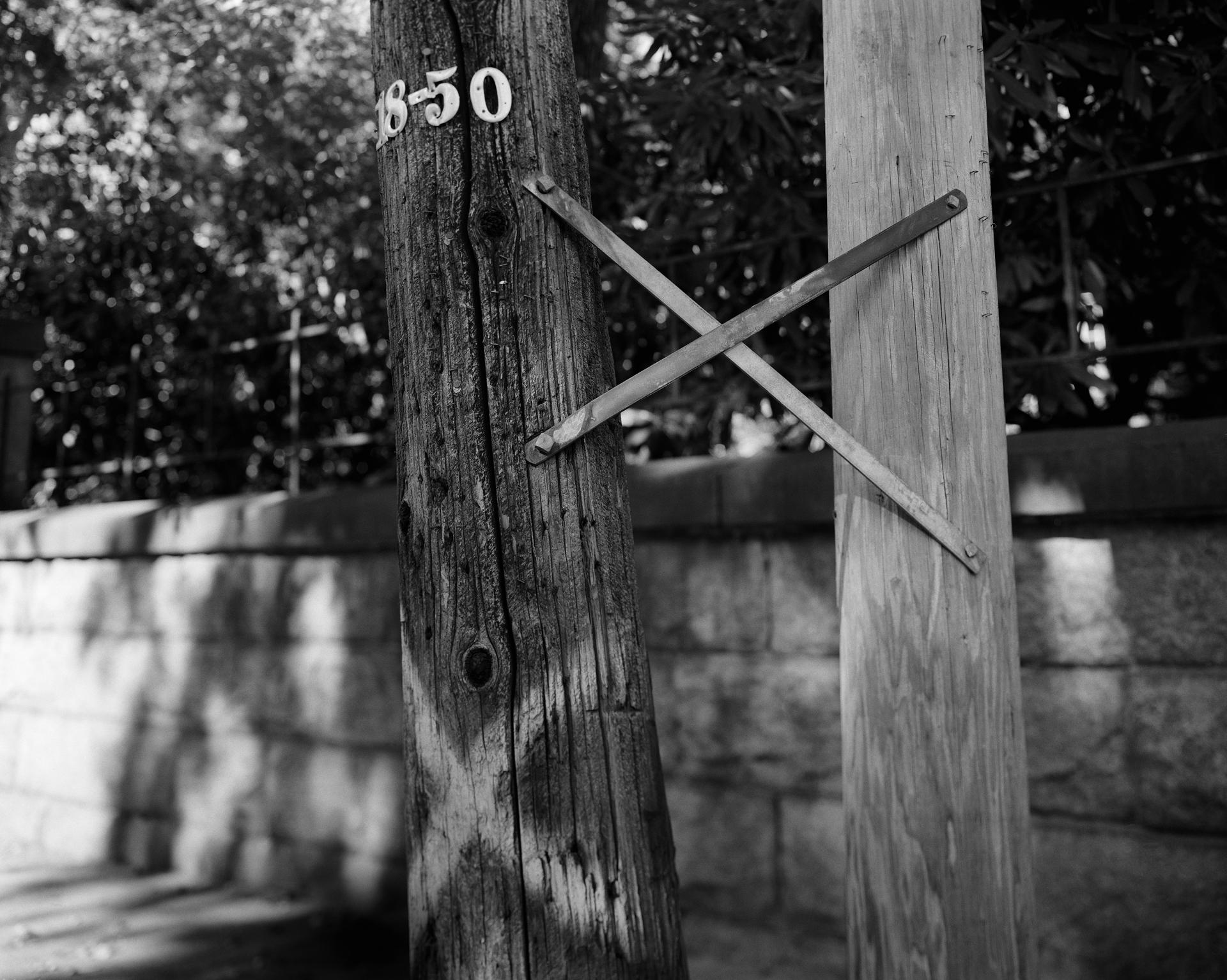 A black and white photograph of two electrical poles bound together with a metal x; one with a painted white x on the lower portion. 