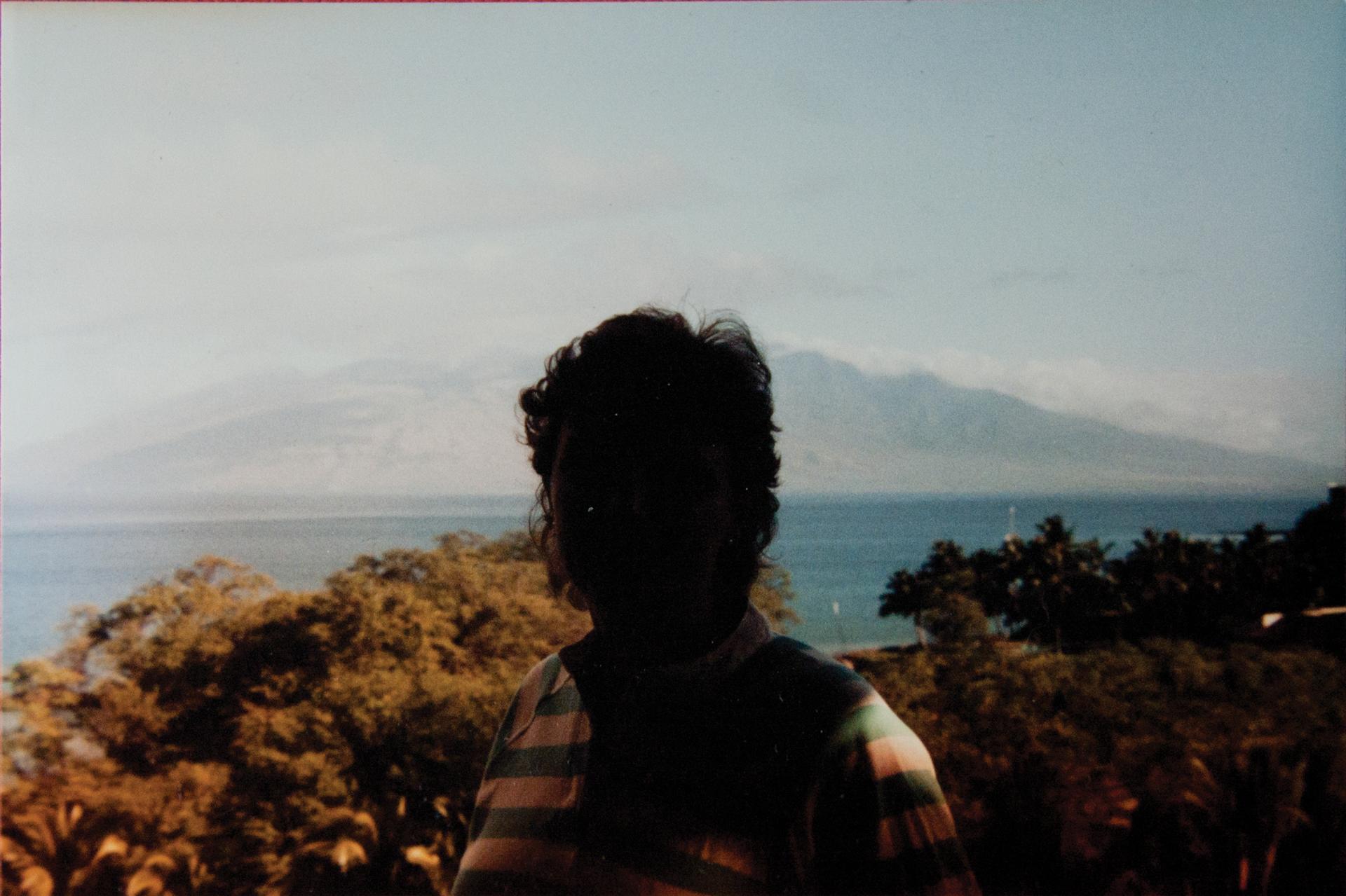 A color photograph in which a landscape can be seen behind a severely underexposed and backlit person.