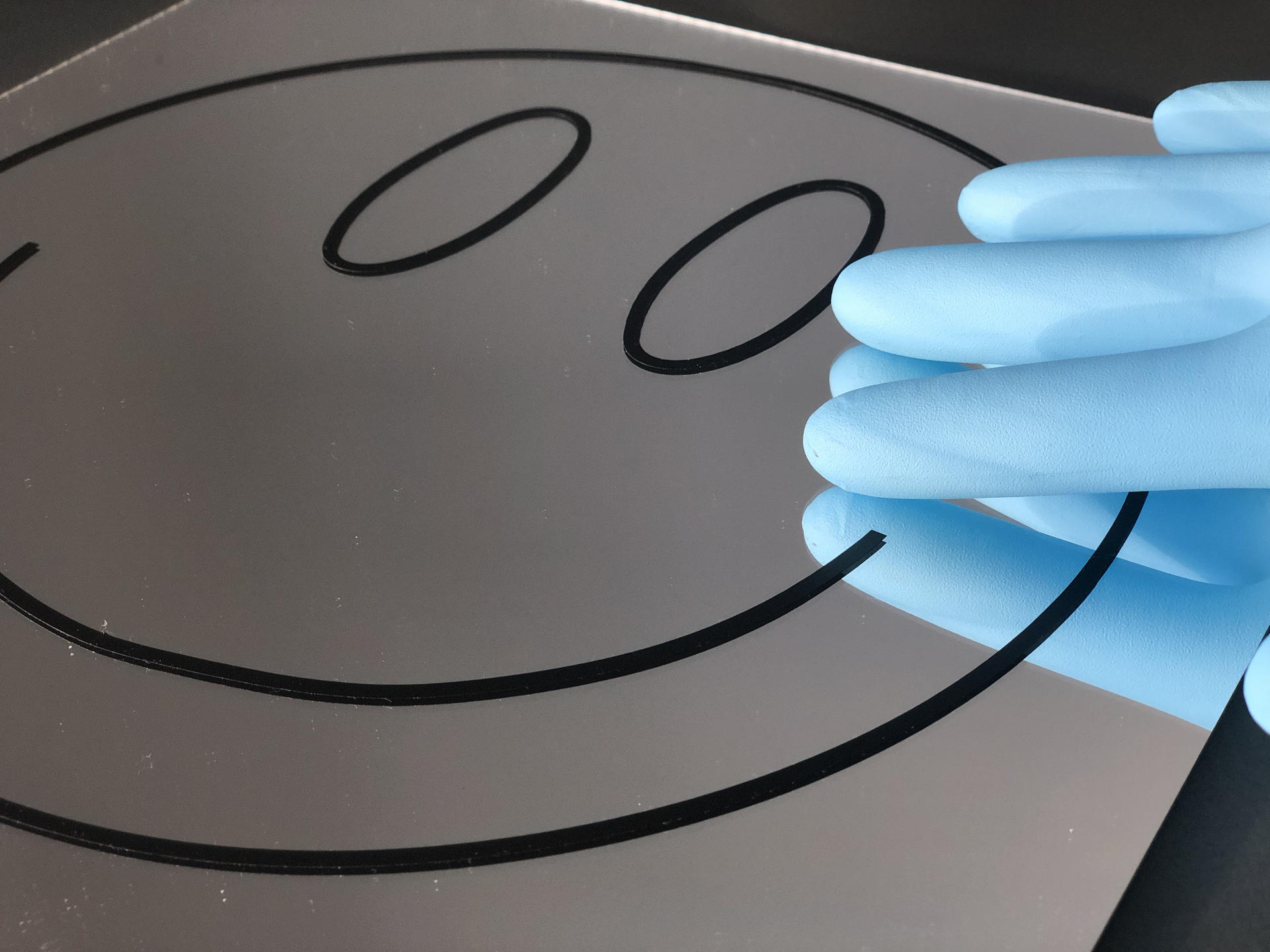 Smiley face graphic on a mirror with a blue-gloved hand