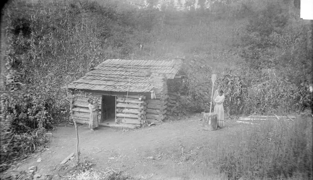 Photograph of Cherokee Medicine Man, Ayunini Swimmer, and his Log Cabin taken by James Mooney (1888).