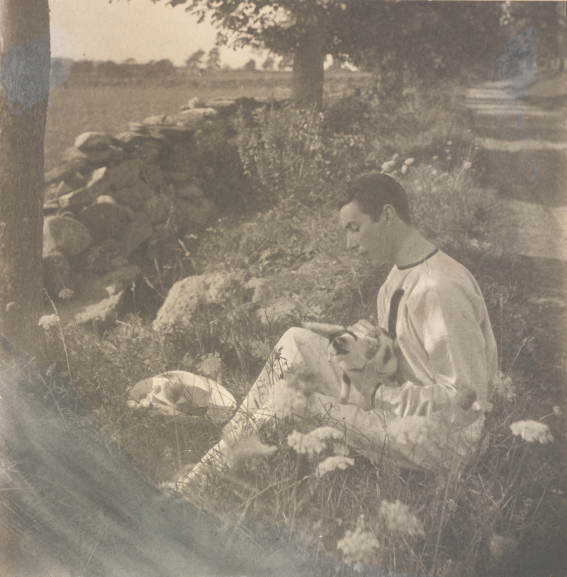 Sepia photograph of a man holding a cat on a country road