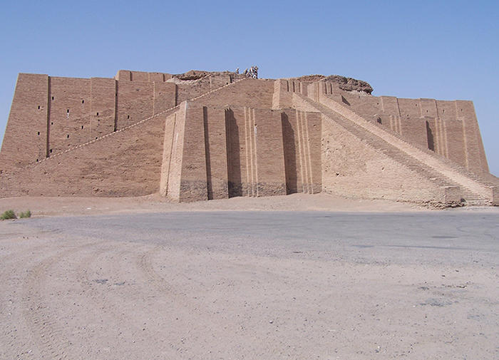 color photograph of the Ziggurat of Ur. Lower half of the photo is beige sand; the upper half is the remains of the Ziggurat and blue sky. The ziggurat a large beige stone rectangular structure with long sloping staircases.