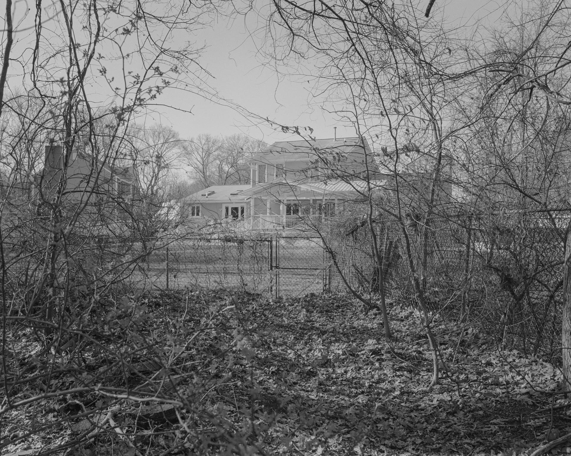 A black and white image of a house in the background hidden in the forest 