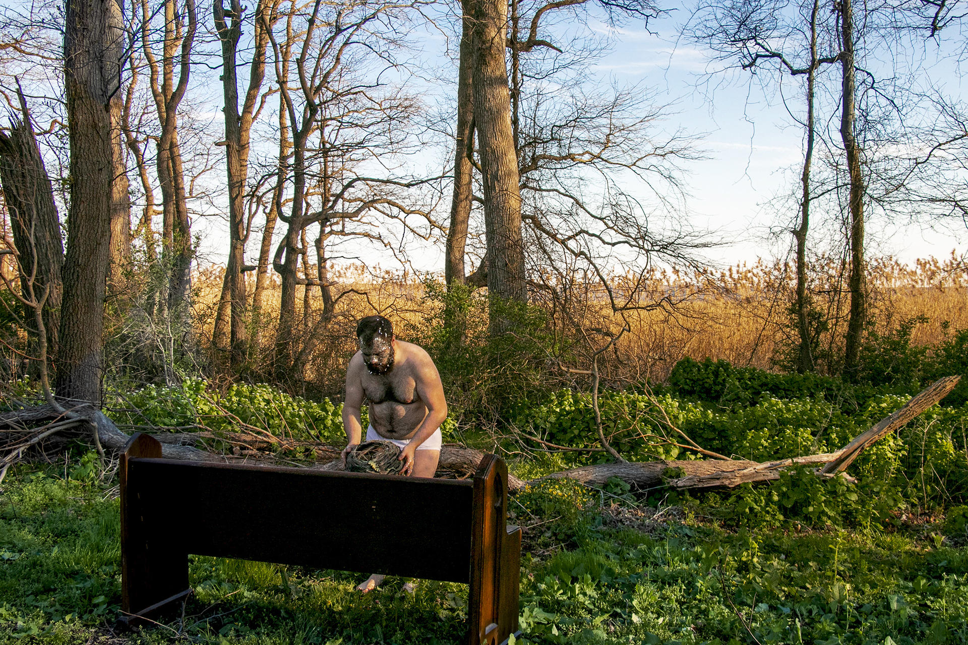 Photograph of artist in forest holding handmade nest made out of clay with plastic  silver confetti on his face. 