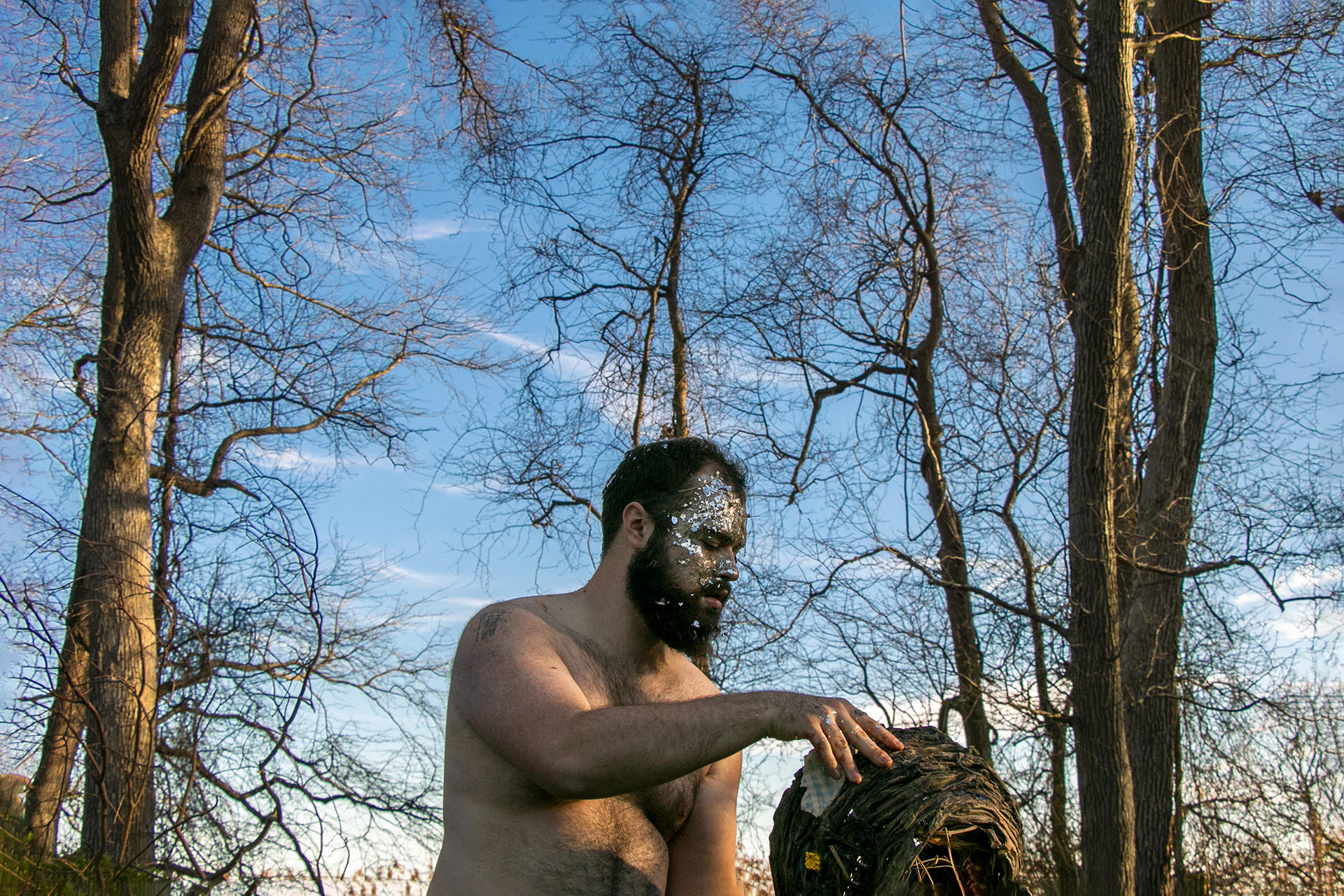 Photograph of artist in forest holding handmade nest made out of clay with plastic  silver confetti on his face. 
