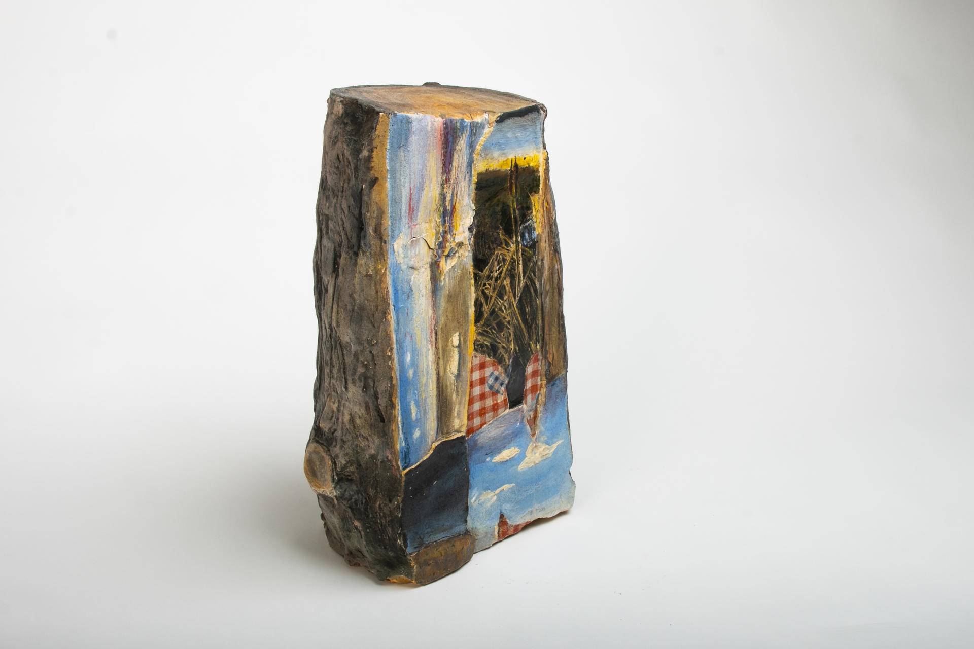 Ceramic piece resembling a cut log. The cut side of log has collaged images of the sea, cattails, and clouds.