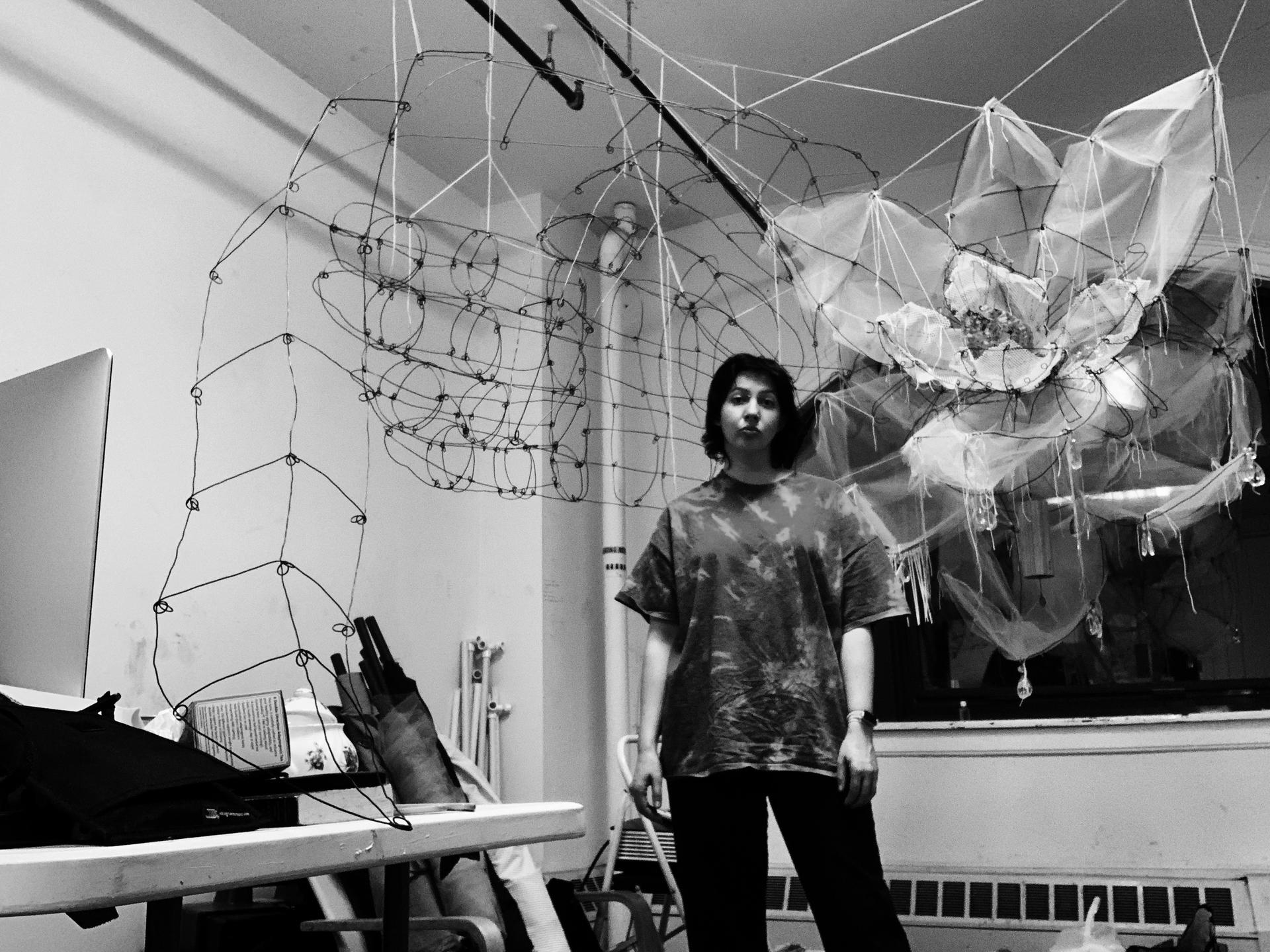 Hannah Suzanna standing in front of some of her partially completed wire sculptures, including a blade of grass, a hand, and a magnolia. - The Ephemeral Altar & The Floating Grave - Hannah Suzanna