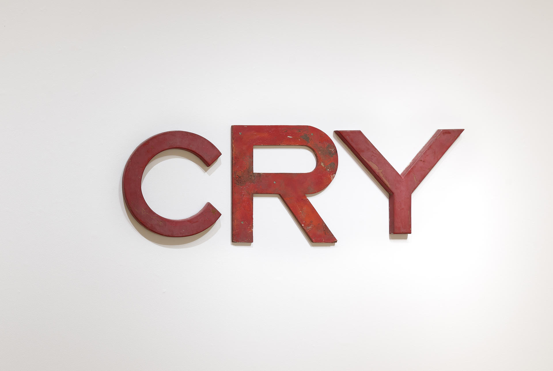 Slightly mismatched red san-serif letters mounted to a wall. They spell the word CRY.